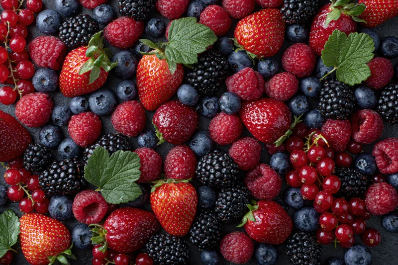 Mixed fresh berries arranged in dense overhead flat lay on dark surface