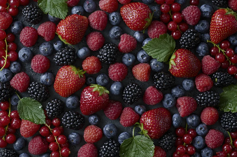 Overhead flat lay of mixed fresh berries densely arranged on dark surface