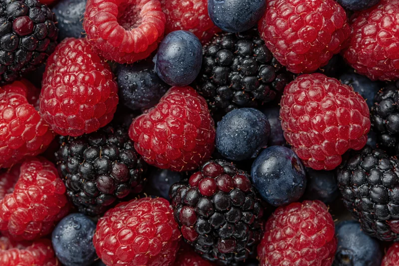 Overhead closeup of mixed fresh raspberries blueberries and blackberries arranged flat on surface