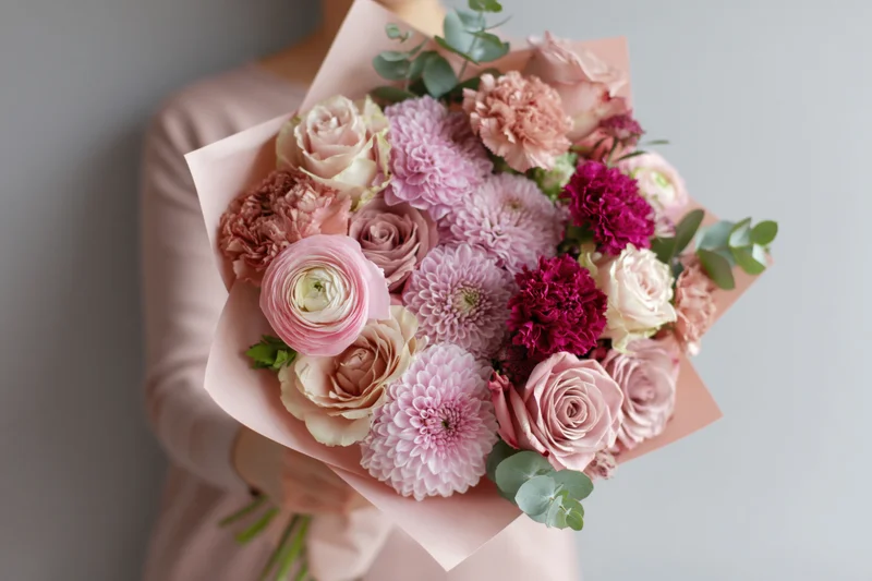 Woman holding a large mixed flower bouquet wrapped in blush paper