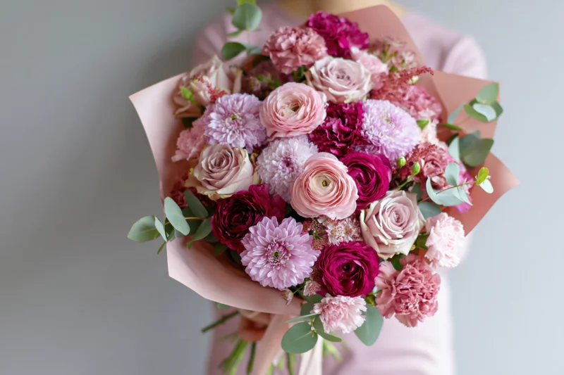Woman holding a large mixed flower bouquet wrapped in blush paper