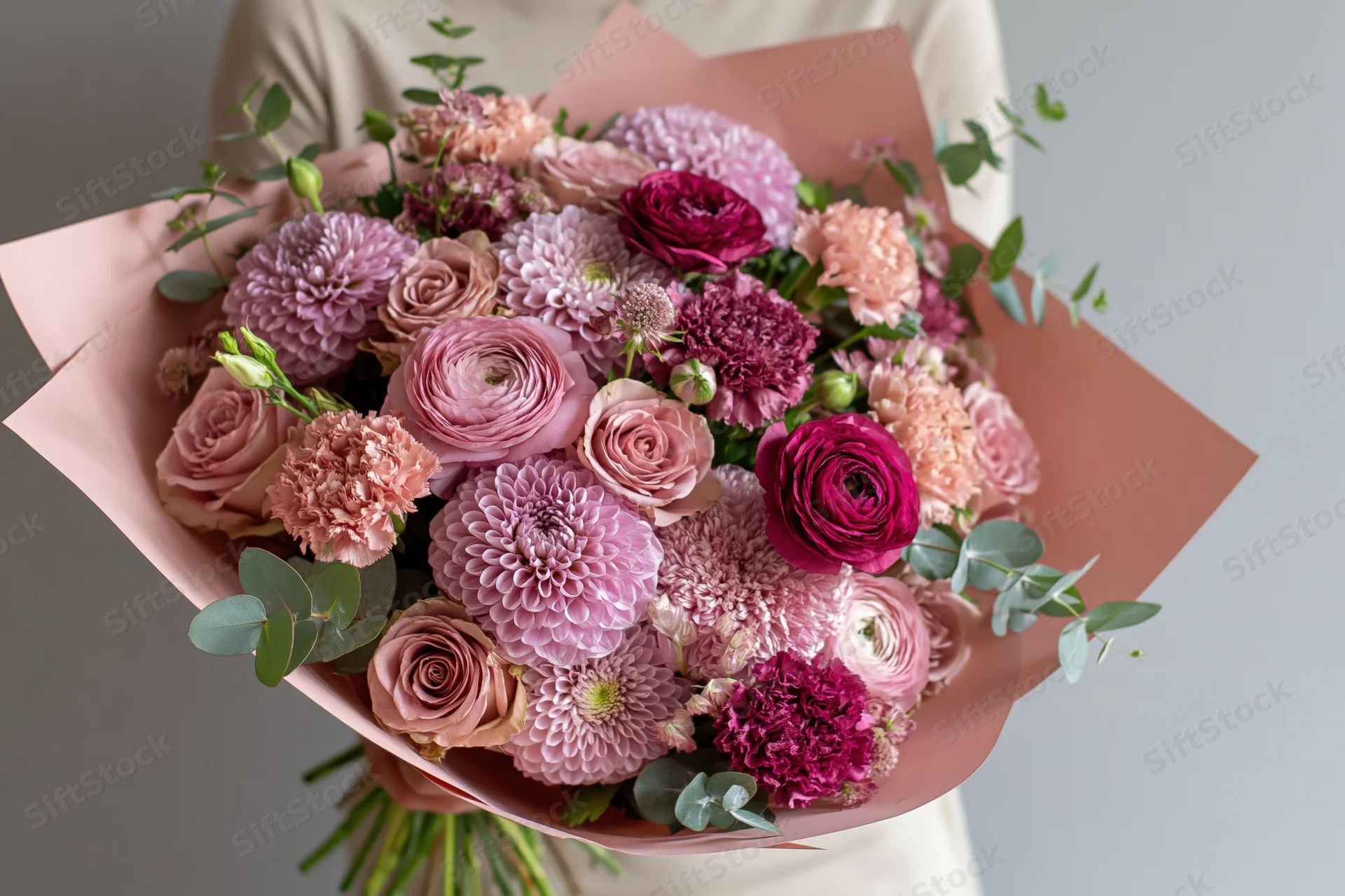 Person holding a large mixed flower bouquet wrapped in blush paper
