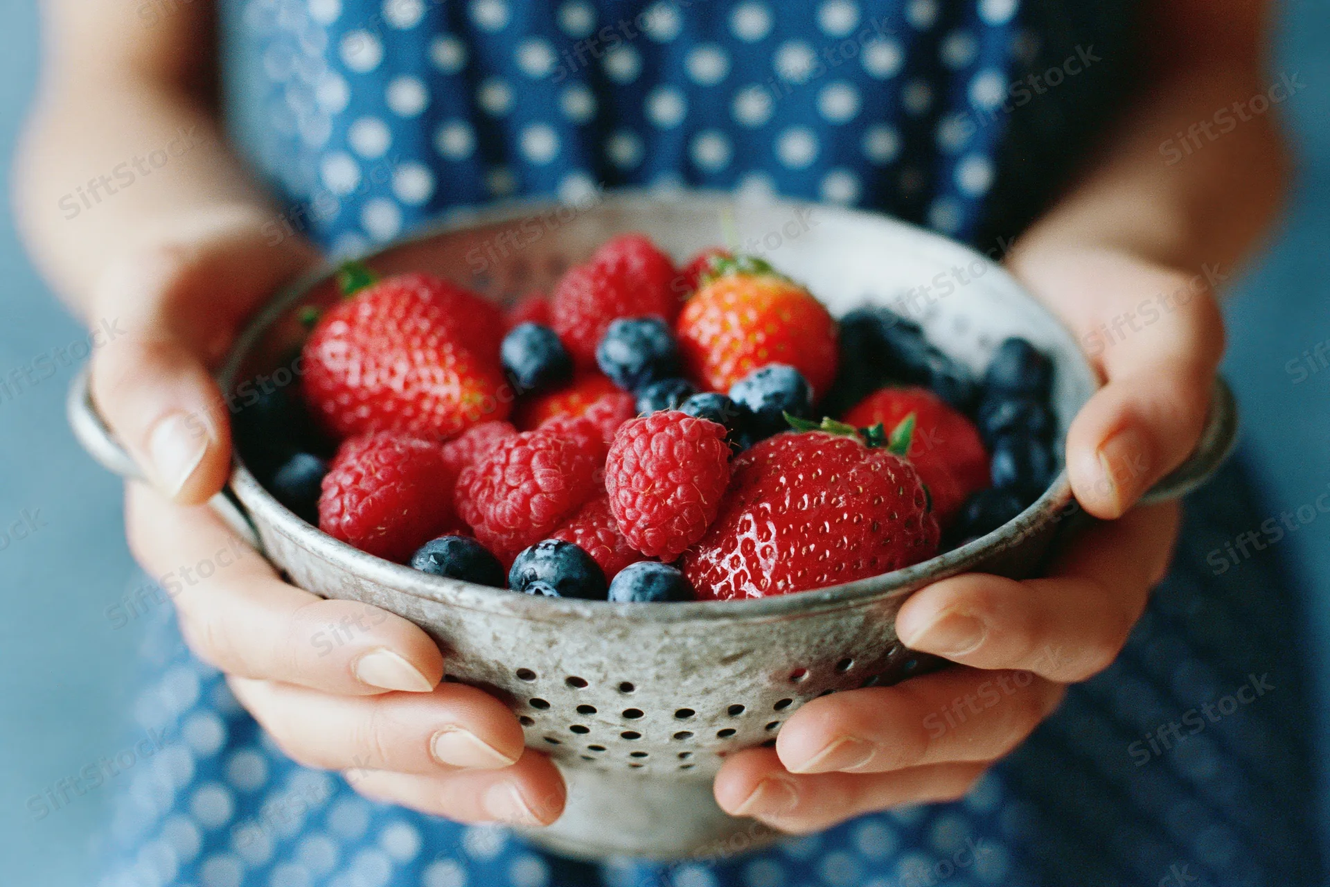 Woman holding a metal colander filled with fresh strawberries, raspberries and blueberries