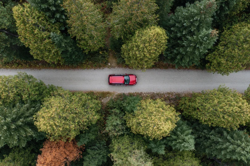 Red suv driving along narrow dirt road through dense forest from above