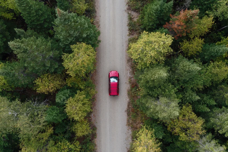 Red suv driving along narrow dirt road through forest from overhead view