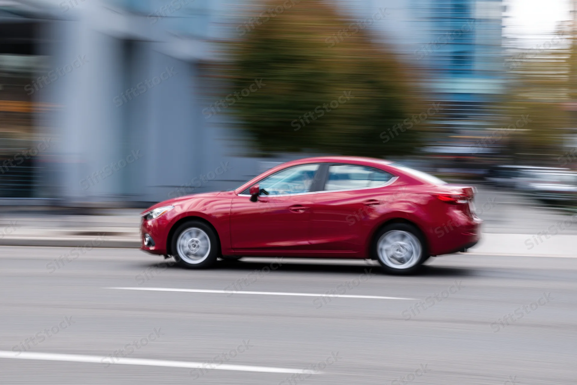 Red compact sedan moving along urban street with motion blur