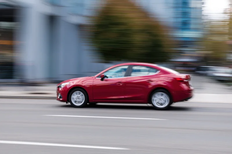 Red compact sedan moving along urban street with motion blur