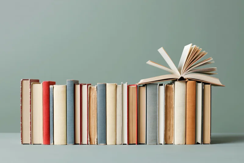 Row of hardcover books standing upright with one open on top against a gray background