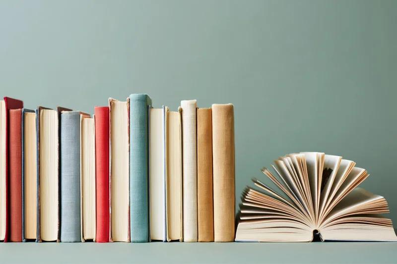 Row of hardcover books standing upright with one open and fanned on a flat surface