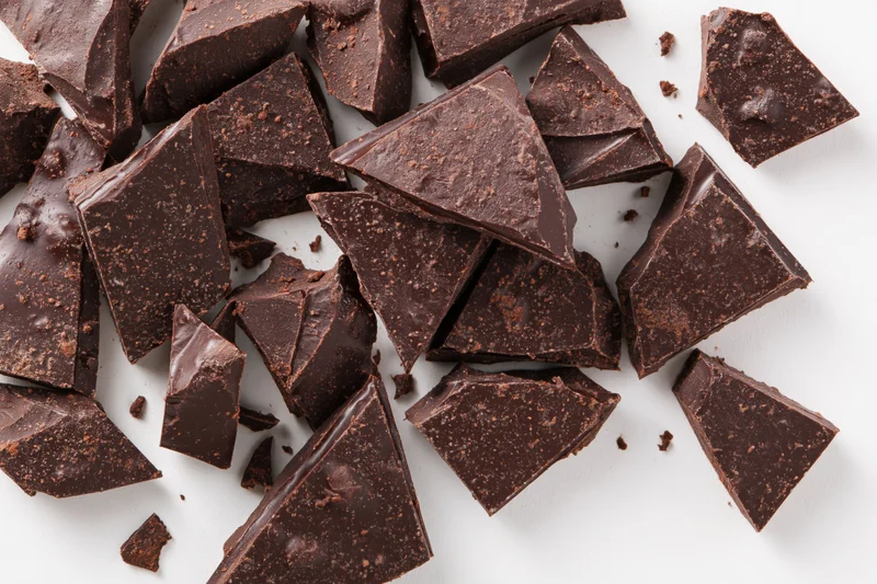 Broken dark chocolate chunks scattered on white background
