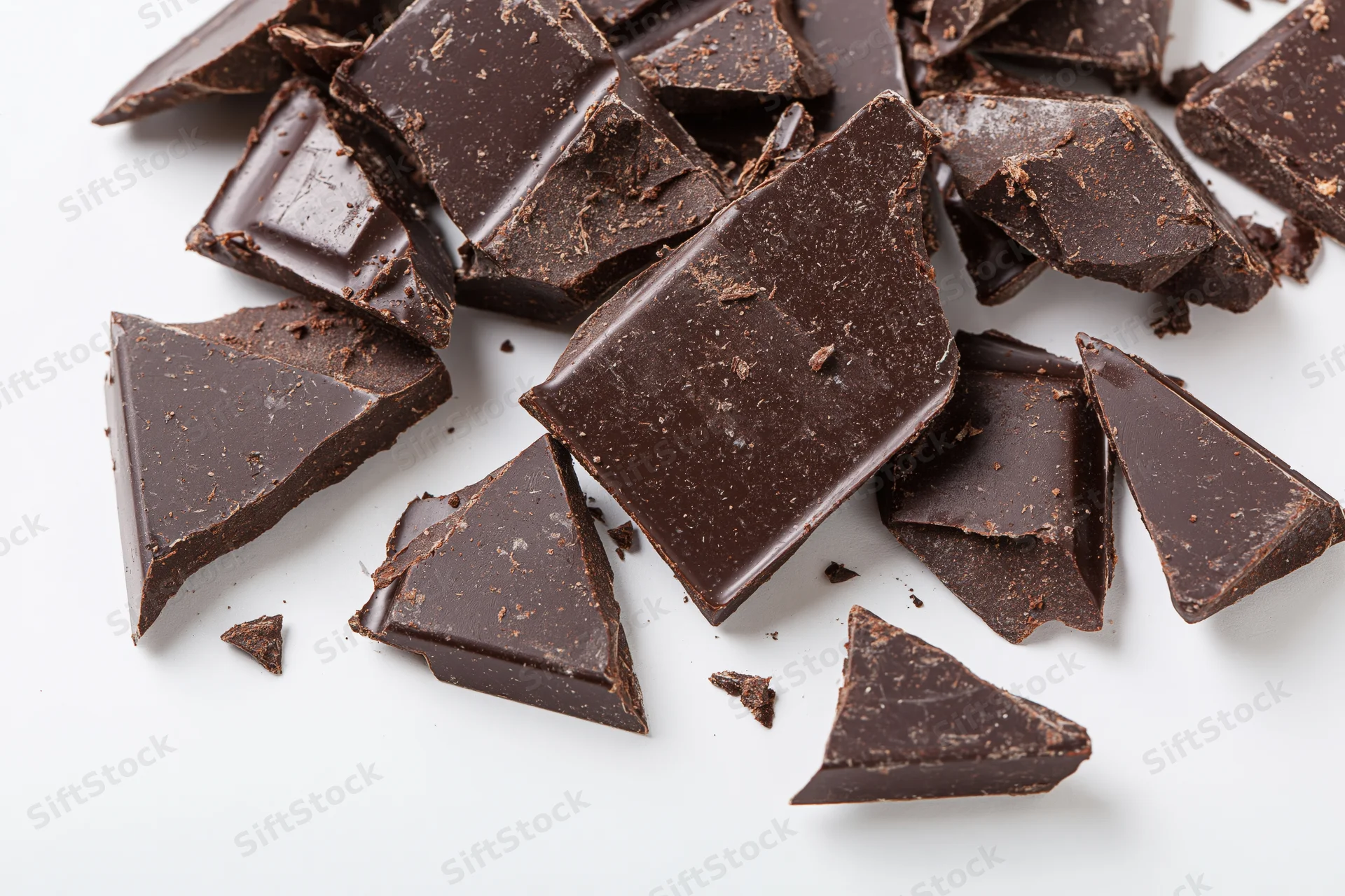 Broken dark chocolate chunks scattered on white background