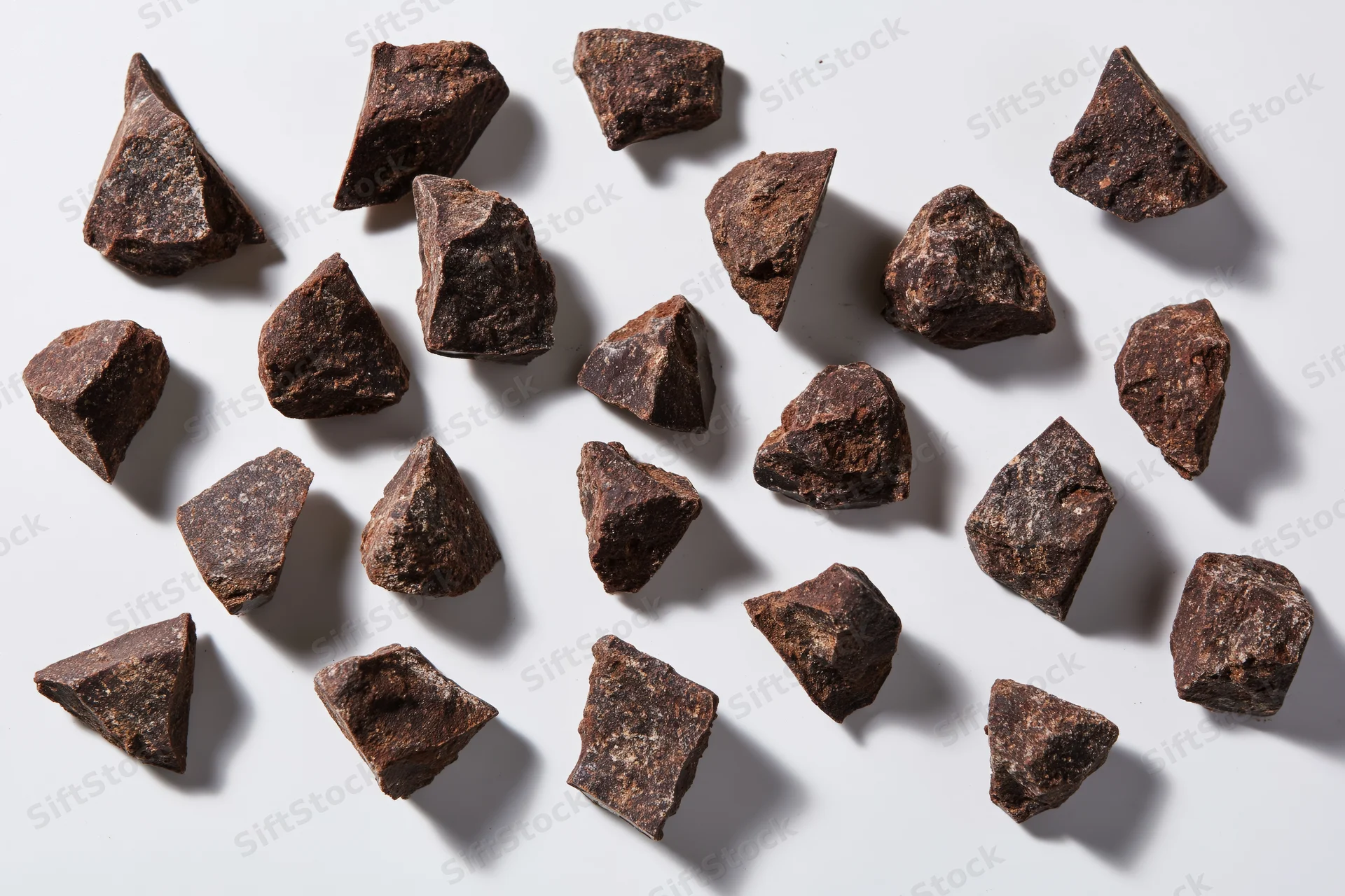 Broken dark chocolate chunks scattered across a white surface in a flat lay arrangement
