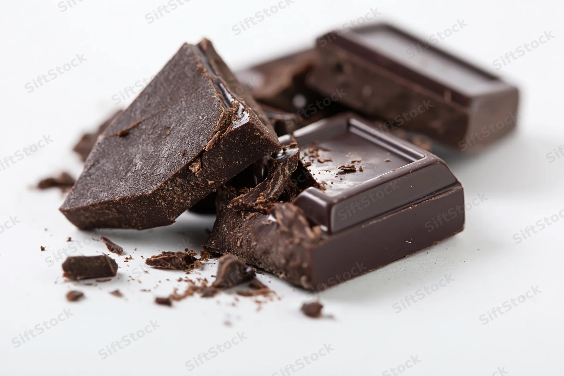 Broken dark chocolate pieces scattered on a white surface