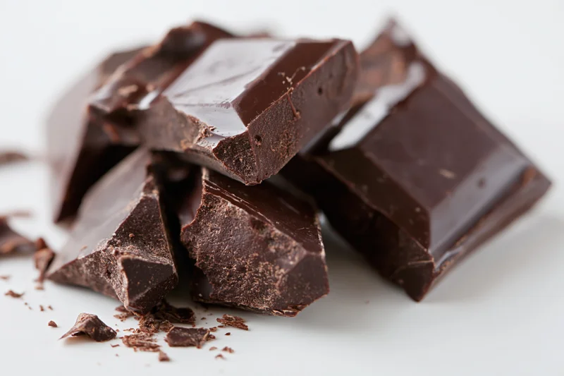 Broken dark chocolate chunks scattered on a white surface