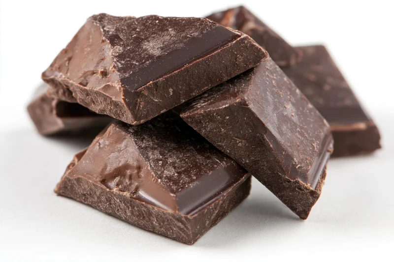 Broken dark chocolate chunks stacked loosely on white background