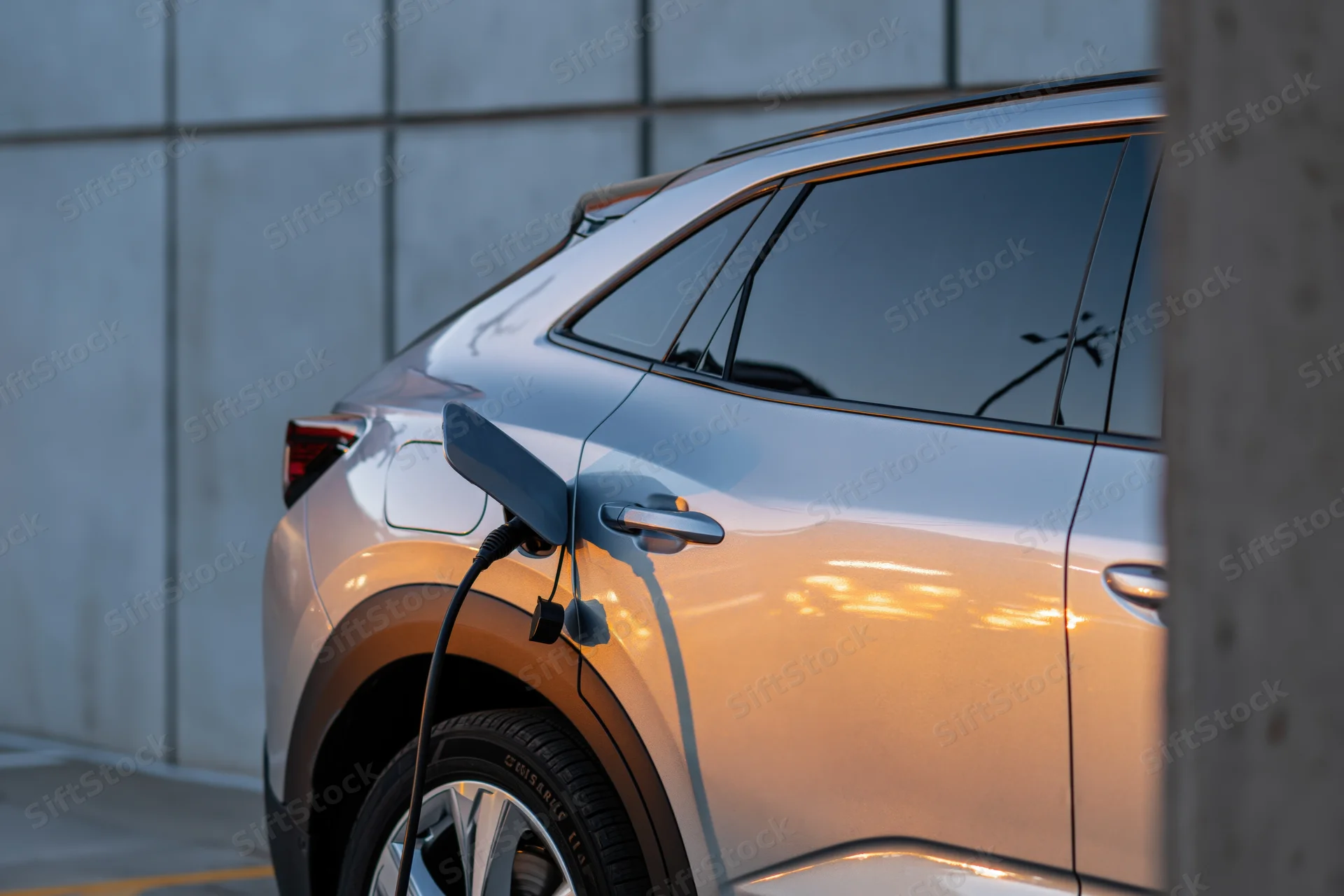 Silver electric suv charging at outdoor station with cable connected to rear port