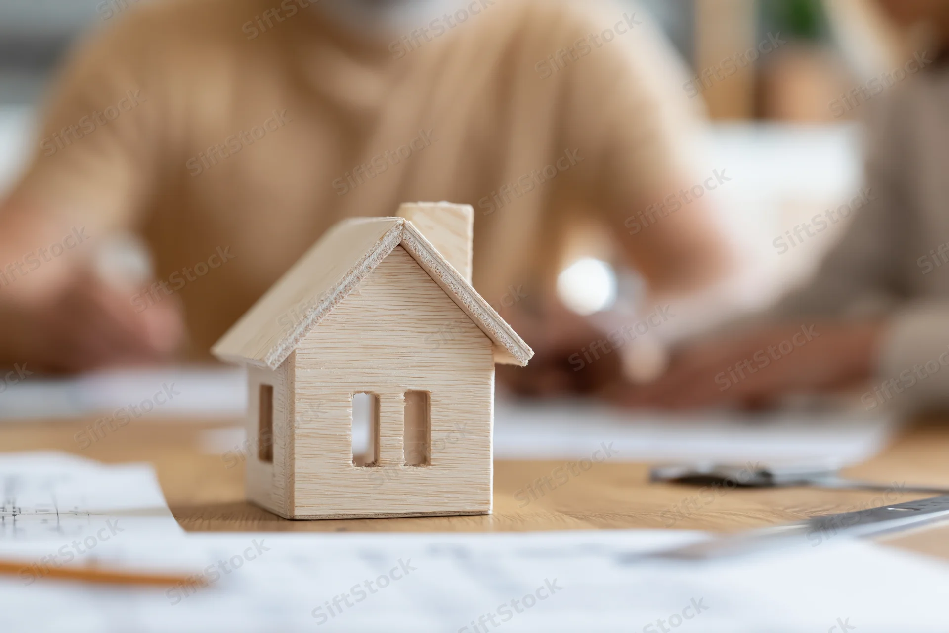 Wooden house model on a desk with blueprints and documents during a real estate meeting