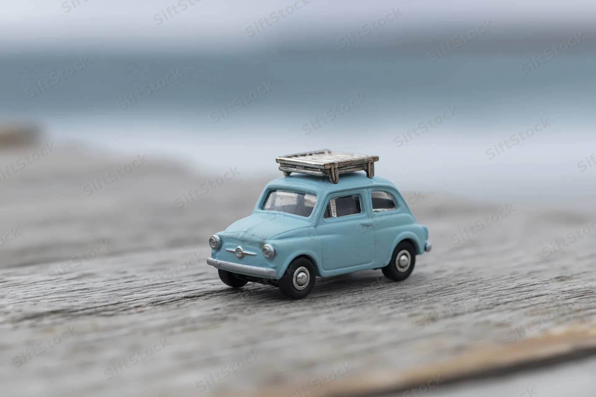 Small blue vintage toy car with luggage rack on weathered wooden deck near ocean