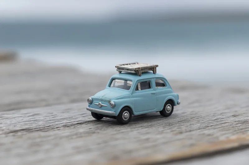 Small blue vintage toy car with luggage rack on weathered wooden deck near ocean