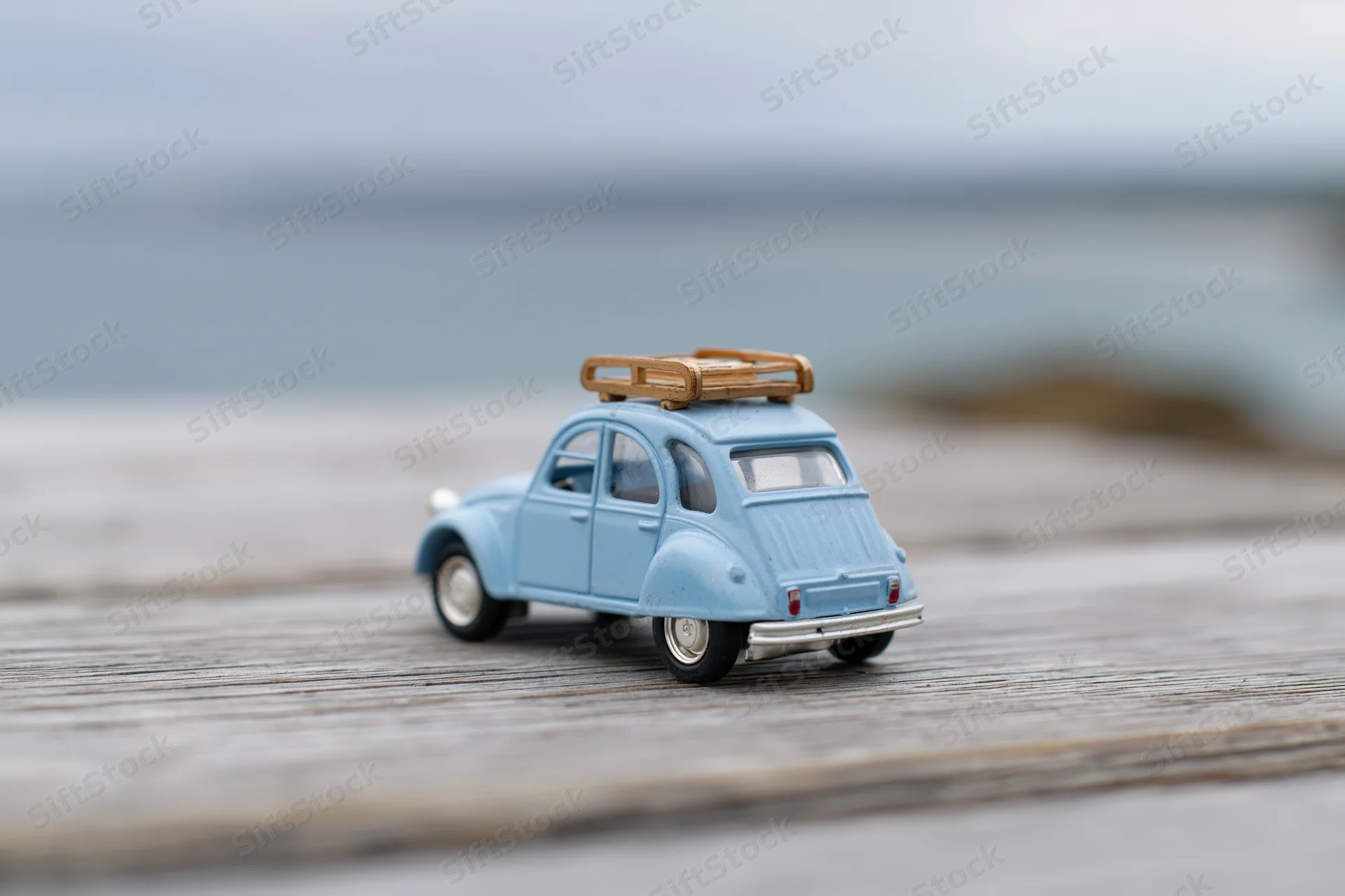 Small blue vintage toy car with wooden luggage rack on wooden deck near water