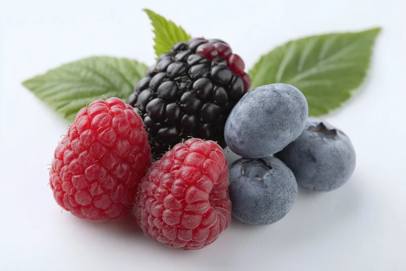 Cluster of fresh raspberries, blackberry and blueberries with green leaves on white background