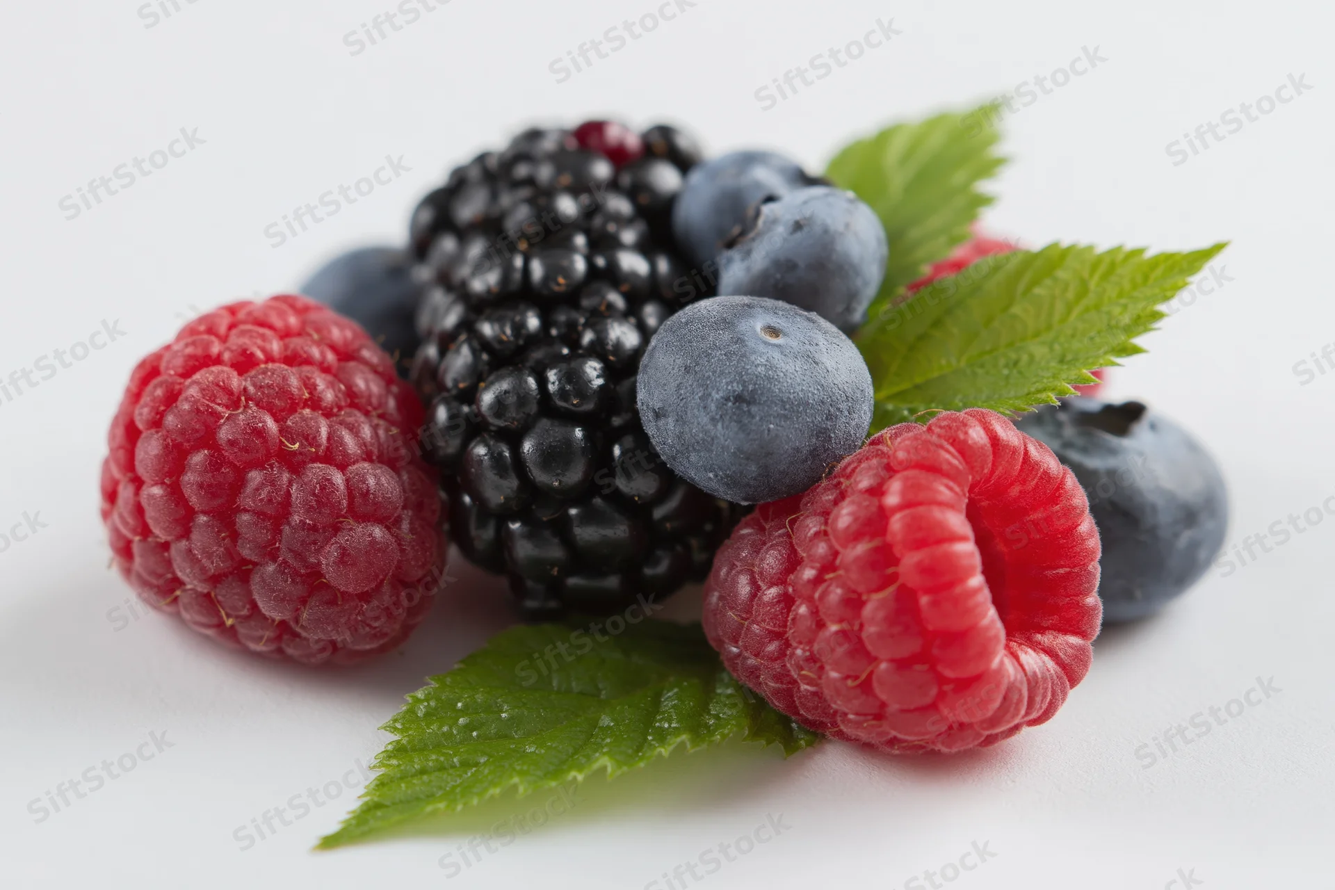 Cluster of fresh raspberries, blackberry and blueberries with green leaves on white background
