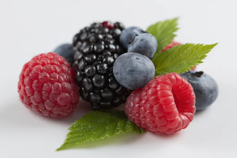 Cluster of fresh raspberries, blackberry and blueberries with green leaves on white background