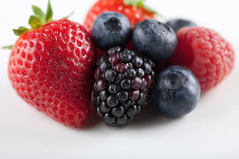 Mixed fresh berries arranged on a flat white surface