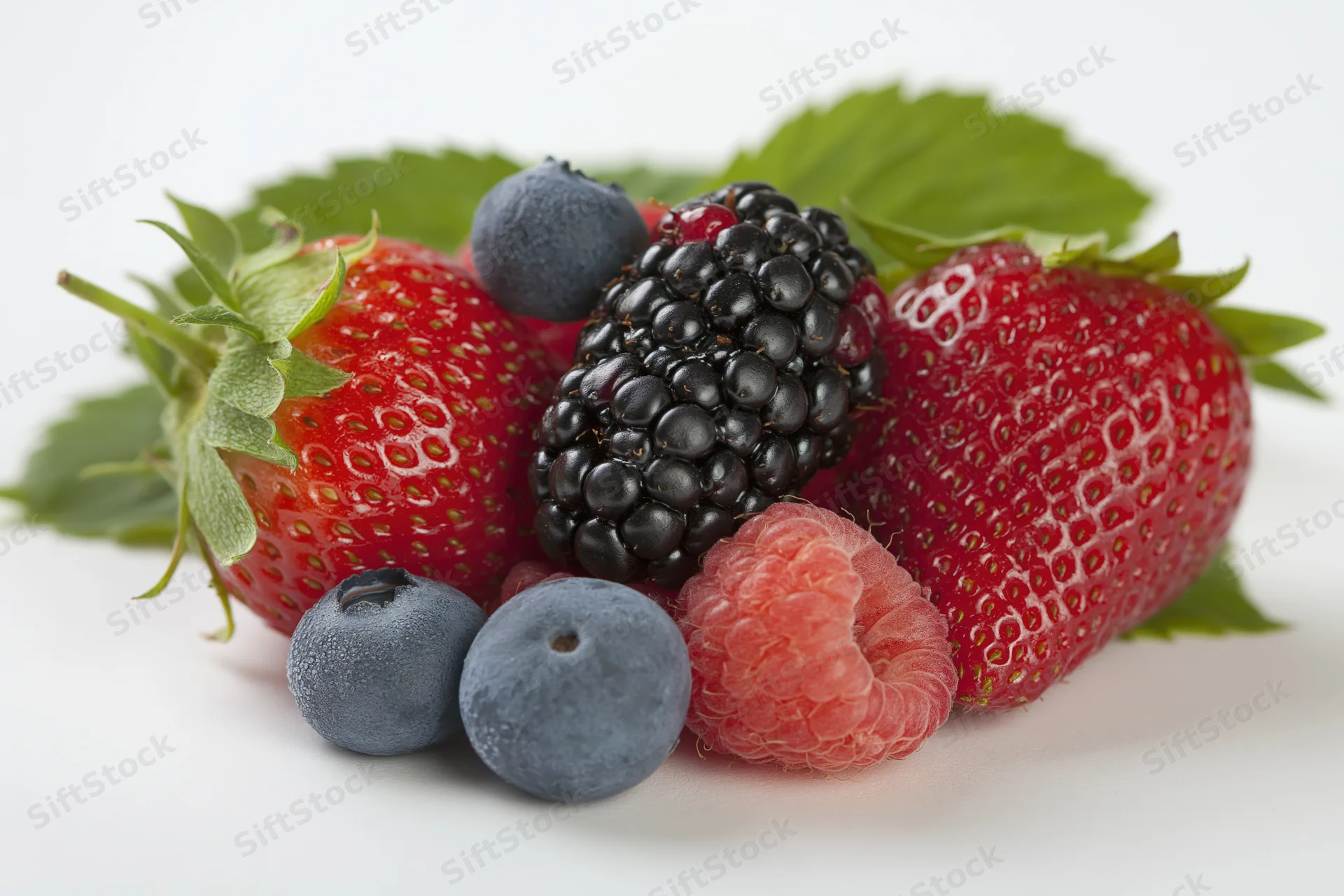 Mixed fresh berries arranged on a white surface with green leaves