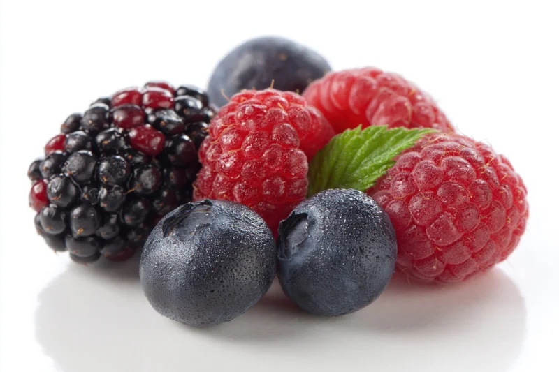 Cluster of fresh blackberries, raspberries and blueberries with a mint leaf on white background
