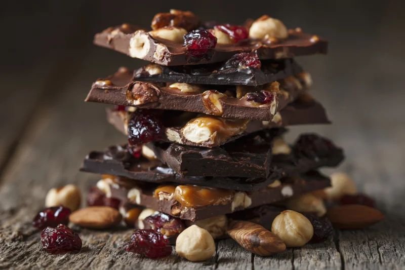 Stack of chocolate bark pieces with hazelnuts, cranberries and caramel on a rustic wooden surface