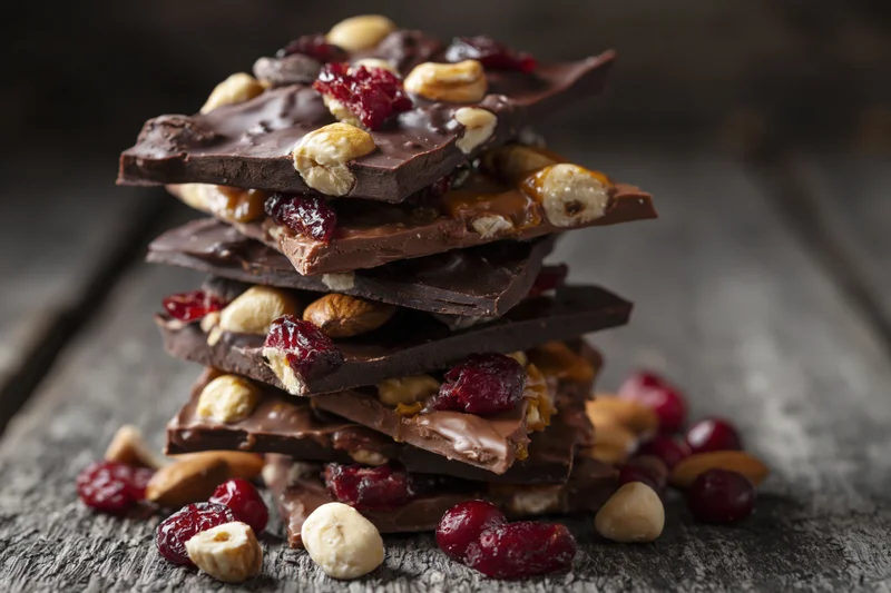 Stack of chocolate bark pieces with nuts and dried cranberries on a rustic wooden surface