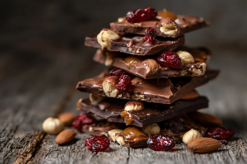 Stack of chocolate bark pieces with nuts and dried fruit on wooden surface