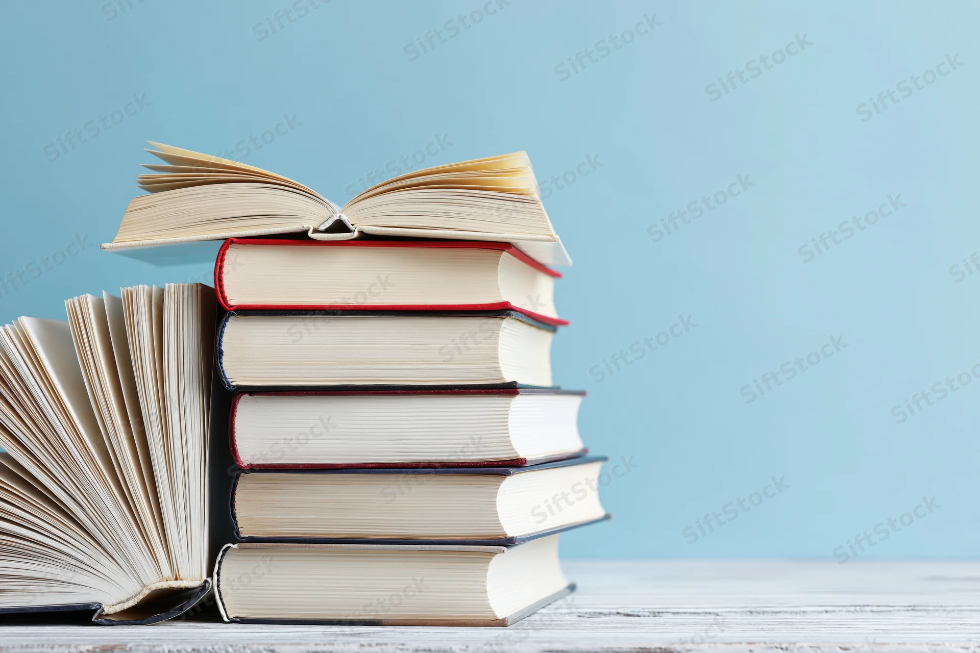 Stack of open hardcover books on a white wooden surface with blue background