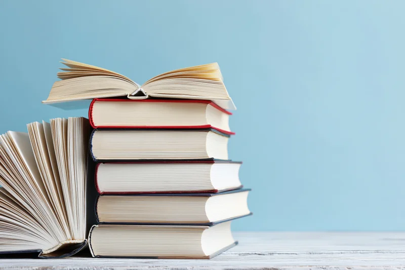 Stack of open hardcover books on a white wooden surface with blue background