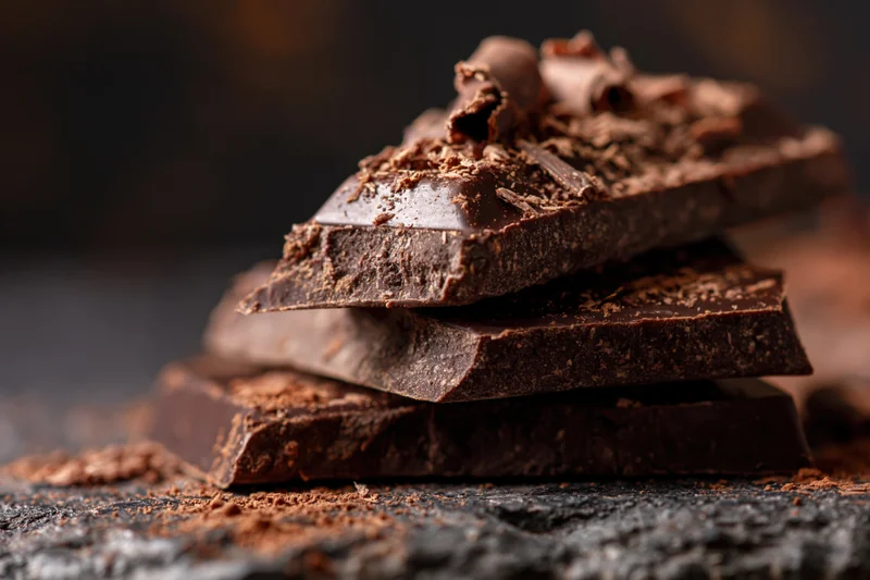Broken dark chocolate pieces stacked and topped with shavings on a dark slate surface