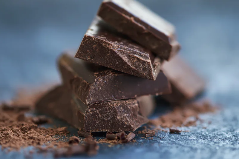 Broken dark chocolate pieces stacked loosely on a slate surface with cocoa powder scattered around