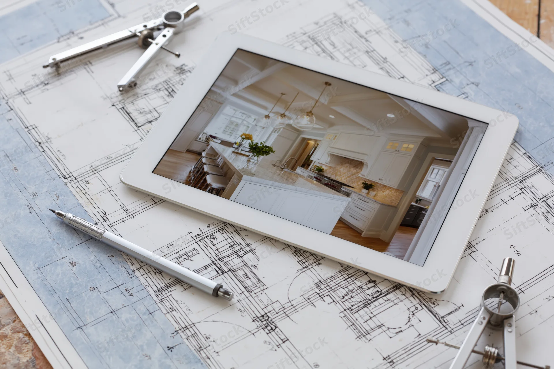 Tablet displaying kitchen interior photo on top of architectural blueprints with drafting tools around