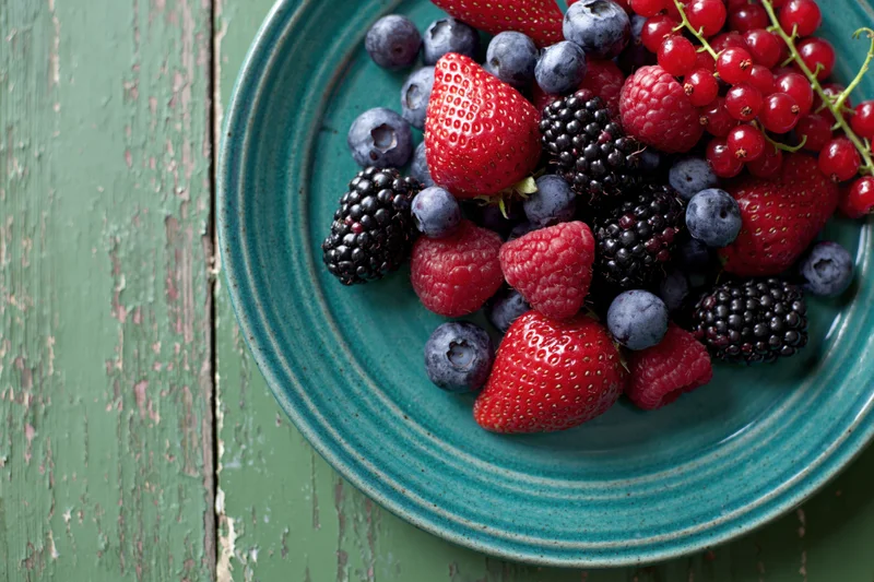 Mixed fresh berries on a teal ceramic plate on a rustic green wooden table
