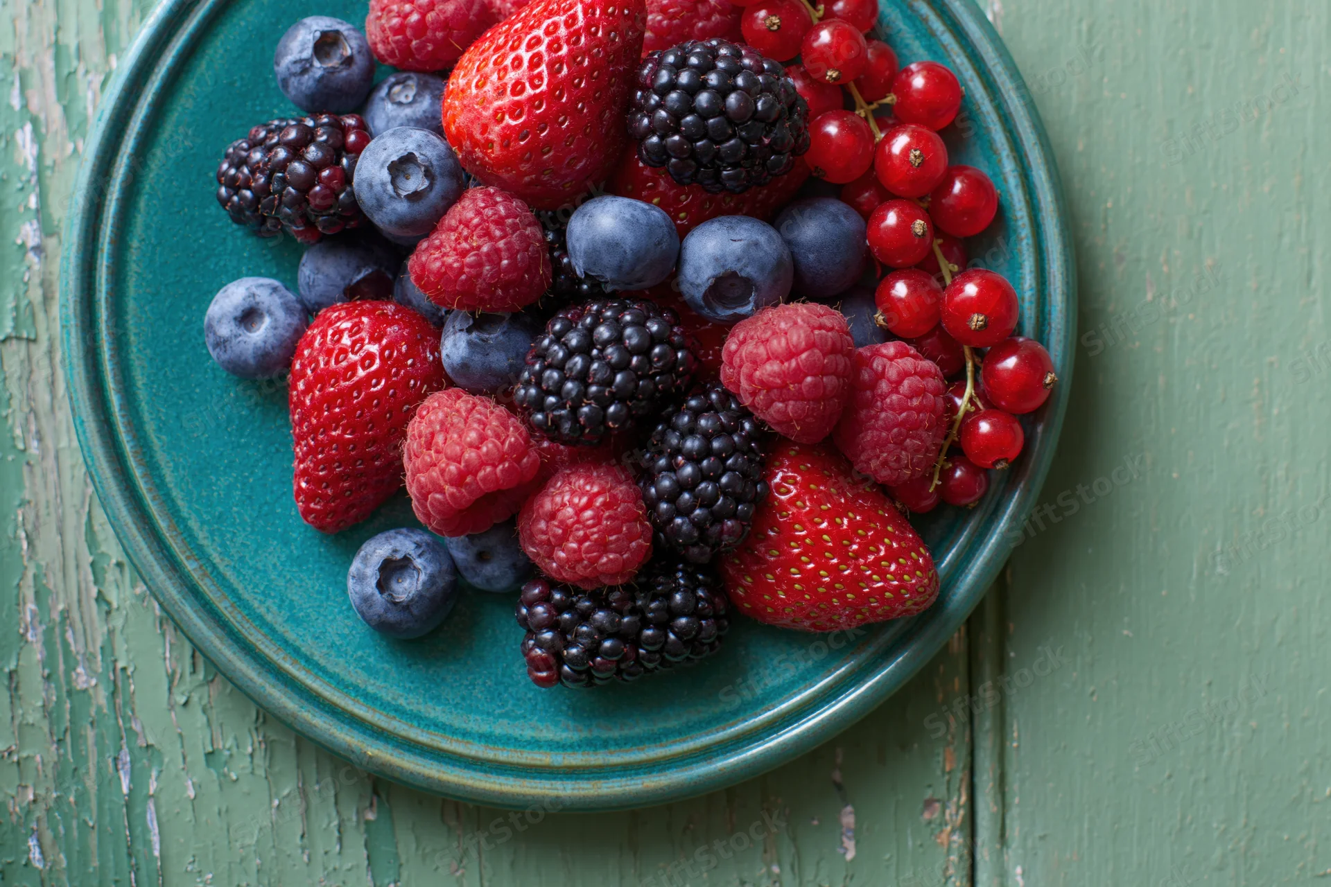 Mixed fresh berries piled on a teal ceramic plate on a rustic wooden surface