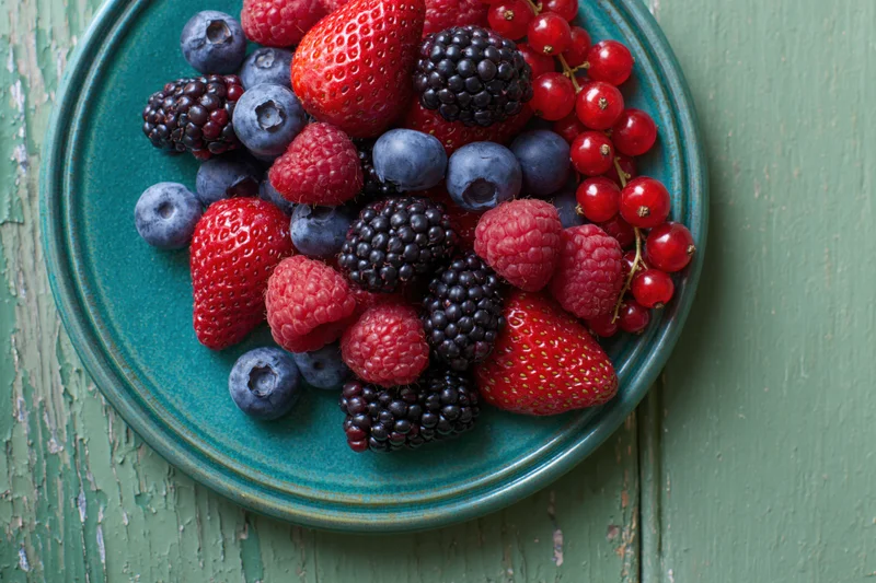 Mixed fresh berries piled on a teal ceramic plate on a rustic wooden surface