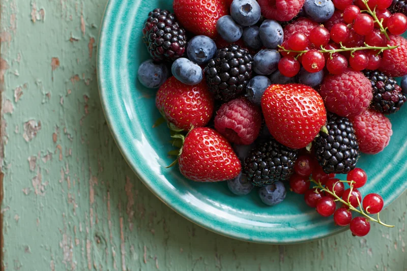 Mixed fresh berries on a teal ceramic plate on a rustic wooden surface