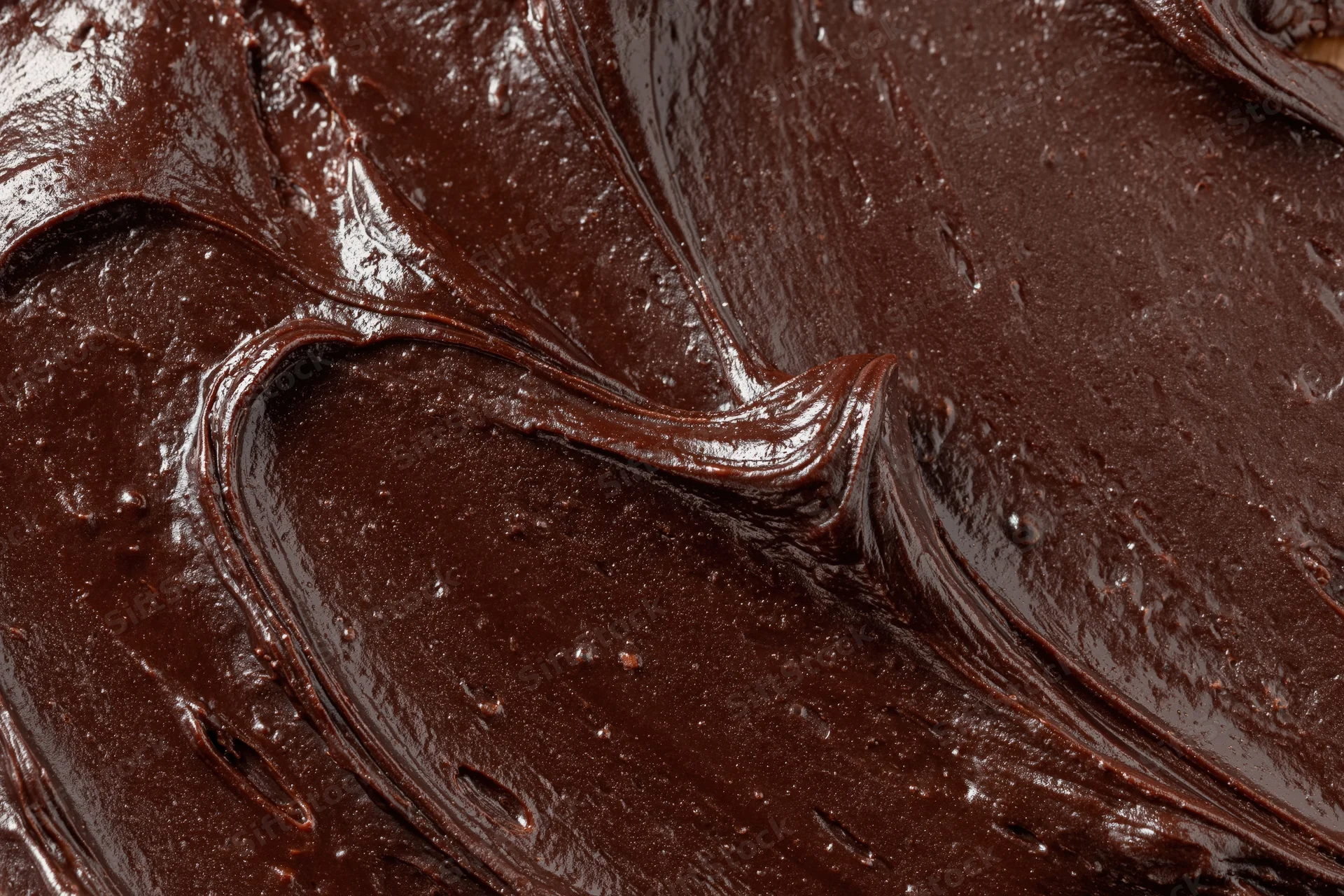Thick dark chocolate ganache spread across a flat surface in smooth glossy swirls