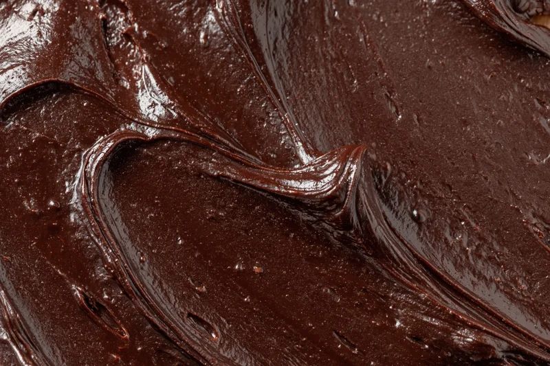 Thick dark chocolate ganache spread across a flat surface in smooth glossy swirls