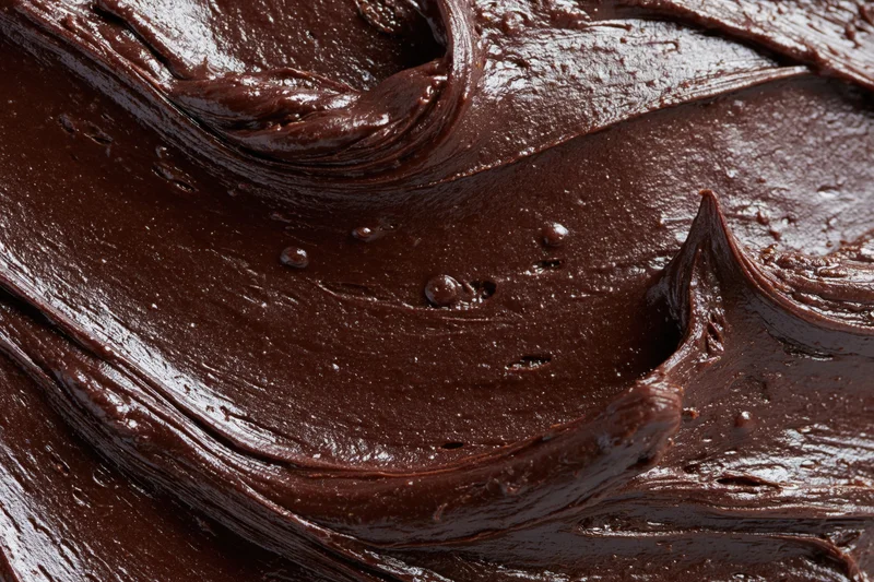 Thick dark chocolate ganache spread in swirling patterns across a flat surface