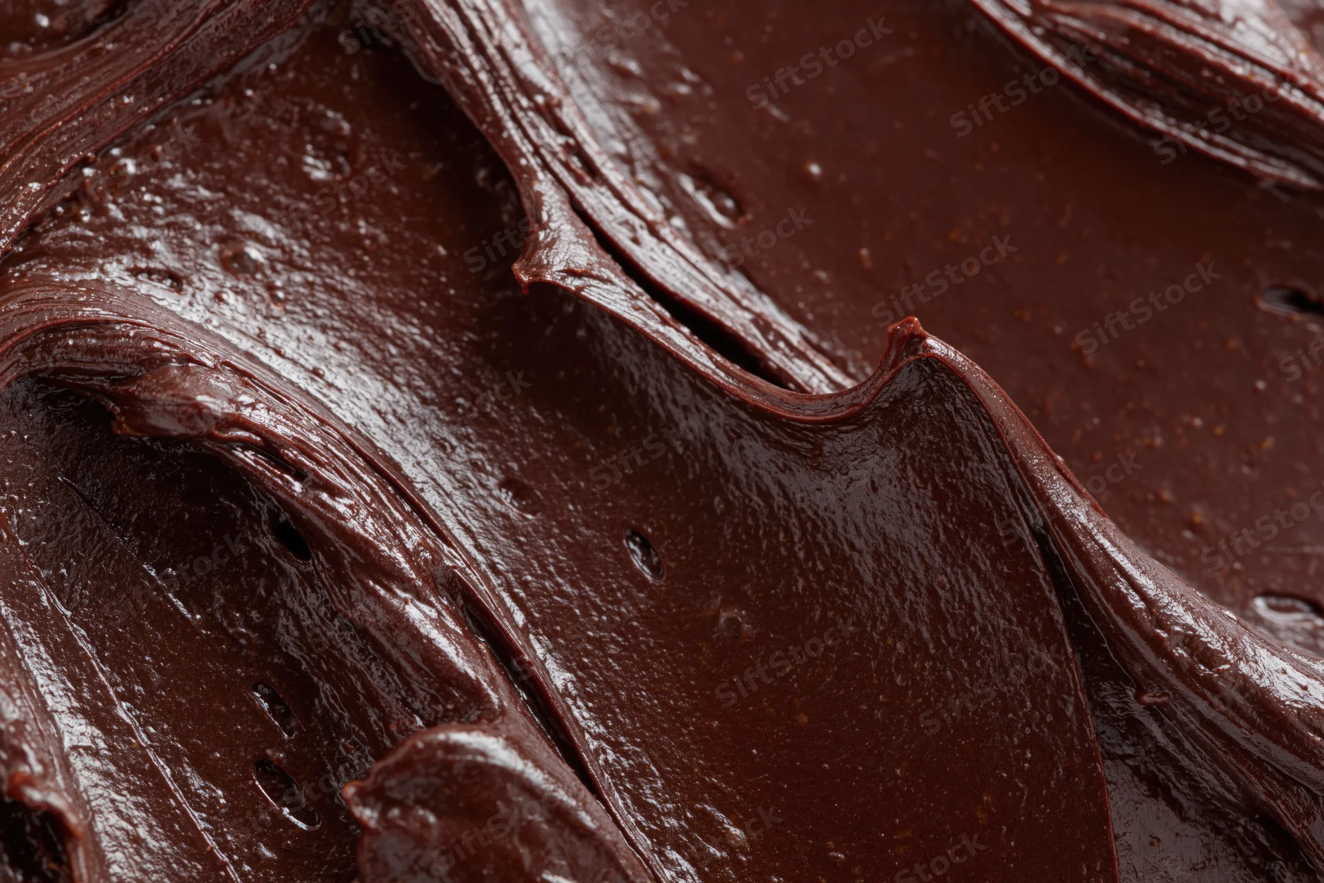 Thick dark chocolate ganache spread in swirling folds across a flat surface
