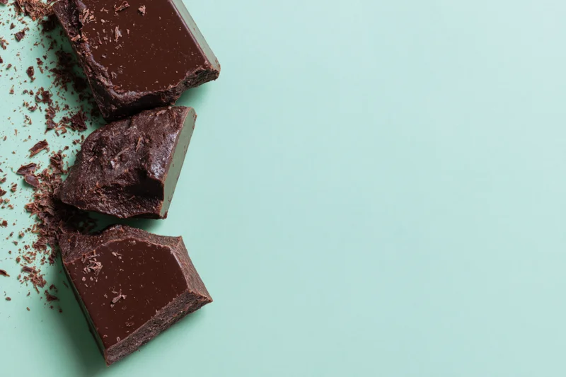 Broken dark chocolate chunks arranged vertically along the left side on a mint green background