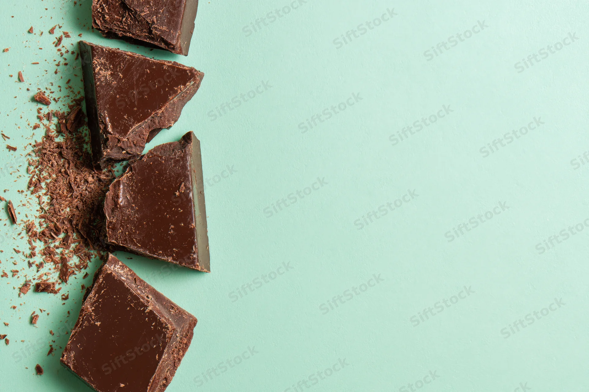 Broken dark chocolate chunks arranged vertically along the left edge on a mint green background with copyspace