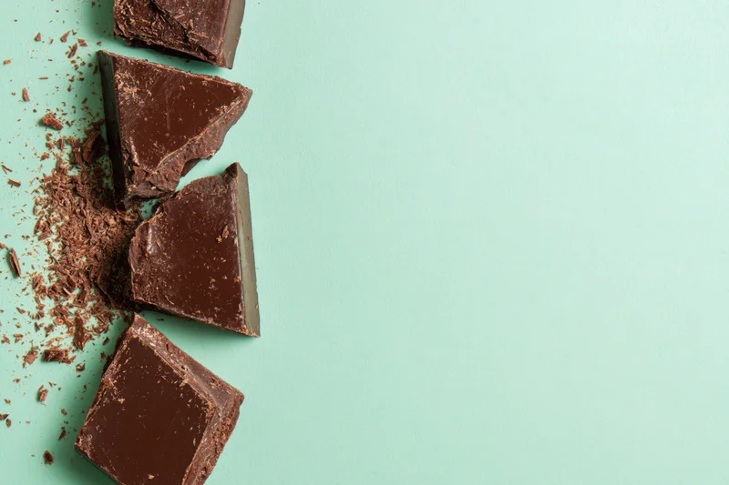 Broken dark chocolate chunks arranged vertically along the left edge on a mint green background with copyspace