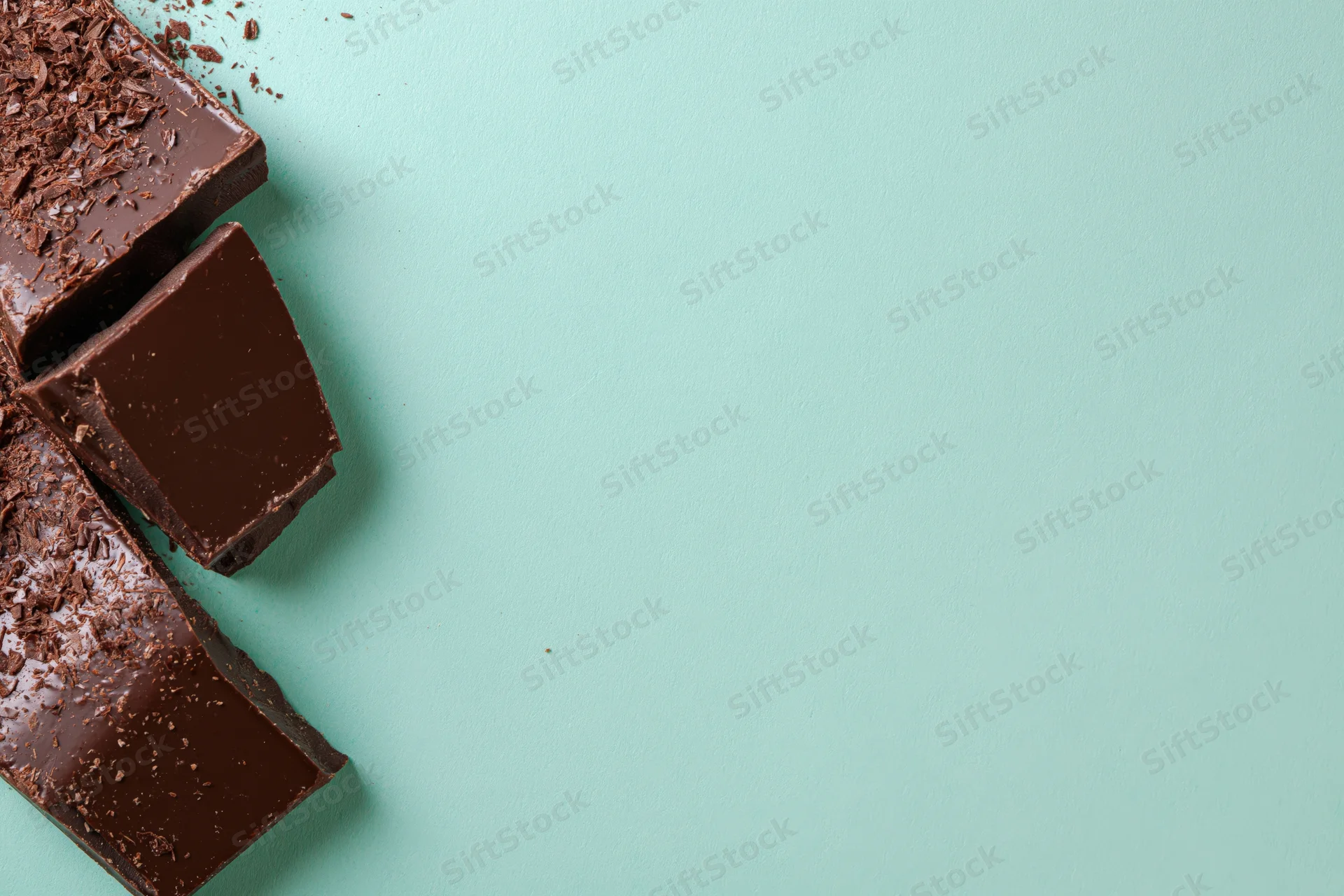 Broken dark chocolate chunks arranged vertically along the left edge on a mint green background with copyspace